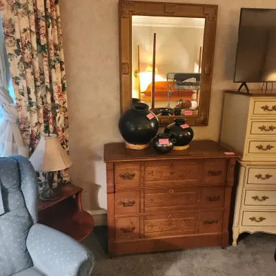 Antique three-drawer dresser with a large carved wall mirror, topped with three black ceramic vessels.