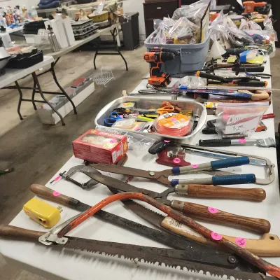 Sale Photo Thumbnail #135: Assortment of hand and power tools, including saws, hedge shears, C-clamps, and a cordless drill displayed on folding tables.