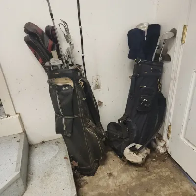 Two vintage golf bags containing assorted clubs and head covers resting against a wall.
