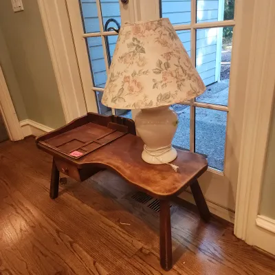 Sale Photo Thumbnail #116: Vintage cobbler bench-style side table with a single drawer and organizer section, topped with a white ceramic lamp featuring a floral patterned shade.