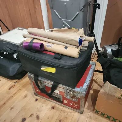 Red and silver road case topped with a black zippered equipment bag and rolls of lighting gels.