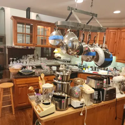 Kitchen filled with cookware and appliances, featuring a ceiling-mounted pot rack with stainless steel pans, countertop blenders, food...