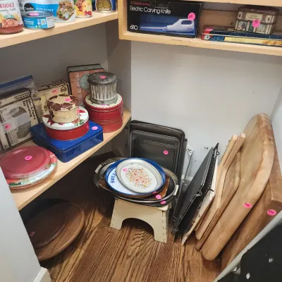 Pantry shelf filled with assorted kitchenware, including decorative tins, a Toastmaster electric carving knife in box, baking sheets, and...