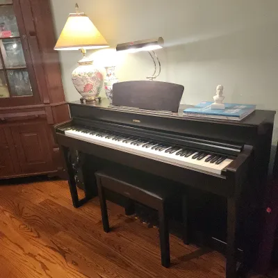 Yamaha digital piano in a dark finish with matching bench, piano light, and music book.
