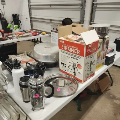 Folding table displays assorted kitchenware, including a stainless steel French press, travel mugs, a vintage fruit and vegetable...
