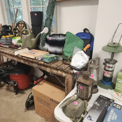 Sale Photo Thumbnail #132: Assorted workshop and outdoor gear including vintage camping lanterns, shop vacuums, a dartboard, watering can, and electronics accessories.