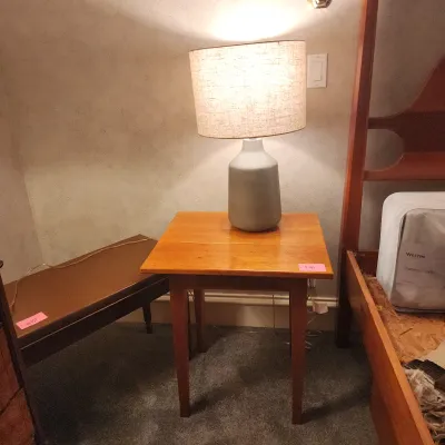 Simple wooden side table with tapered legs, topped with a modern gray ceramic table lamp featuring a textured fabric shade.