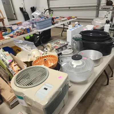 Sale Photo Thumbnail #133: Assortment of household items and kitchenware displayed on folding tables, including a Duracraft humidifier, copper-tone bundt pan, salad spinner, and enamelware roasters.