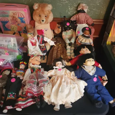 A collection of vintage dolls and plush toys, including a 1980s Teddy Ruxpin plush, various folk costume dolls, porcelain dolls, and a...