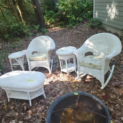 Five-piece white painted wicker patio furniture set, including two rocking armchairs with floral cushions, two accent side tables, and a...