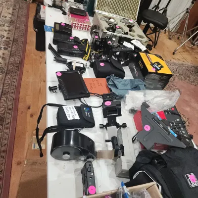 Large collection of vintage camera equipment, accessories, film gear, and monitors displayed on a folding table.