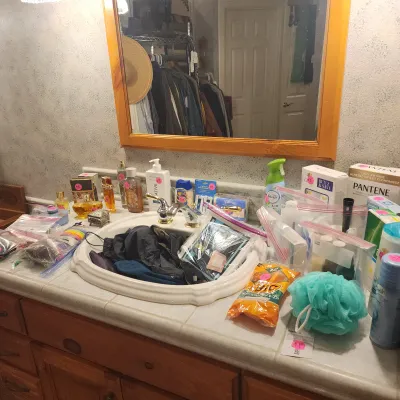 Bathroom vanity counter display featuring various toiletries, perfumes, hair accessories, and personal care items priced for sale.