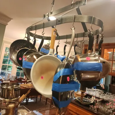 Sale Photo Thumbnail #119: Ceiling-mounted oval wrought iron pot rack hanging over a kitchen island, filled with various cookware including stainless steel saucepans and ceramic-coated skillets.