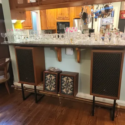 Collection of glassware lined up on a kitchen pass-through counter, with vintage speakers on metal stands displayed below.
