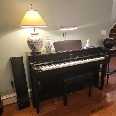 Sale Photo Thumbnail #112: Yamaha digital piano in a dark wood finish with matching bench and brass piano lamp, accompanied by a decorative floral ceramic table lamp.