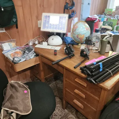 Vintage Apple iMac G4 desktop computer setup on a wooden desk alongside camera equipment, a desktop globe, and various accessories.