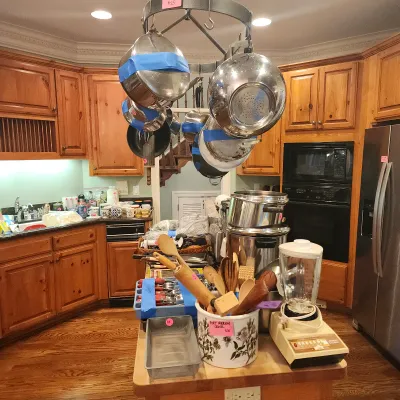 Sale Photo Thumbnail #125: Selection of kitchenware including stainless steel pots on a ceiling-mounted rack, a Portmeirion ceramic utensil crock, vintage blender, and various cooking utensils on an island.