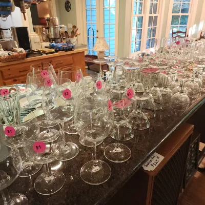 Large collection of assorted clear glassware, including stemware, wine glasses, and goblet cups, displayed on a dark countertop with pink...