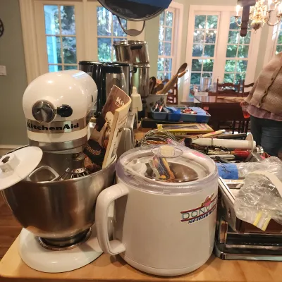 White KitchenAid tilt-head stand mixer with a stainless steel bowl alongside a Donvier ice cream maker and other small kitchen appliances.