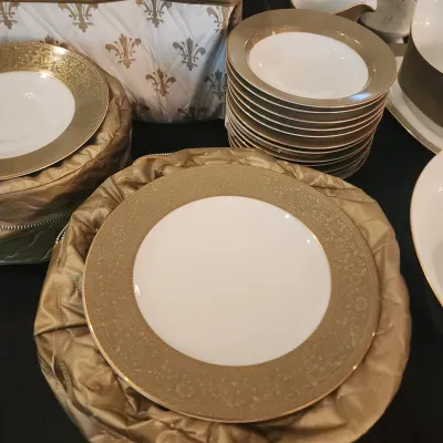 Set of fine porcelain china dishware with ornate gold encrusted borders, stored in quilted gold fabric cases.