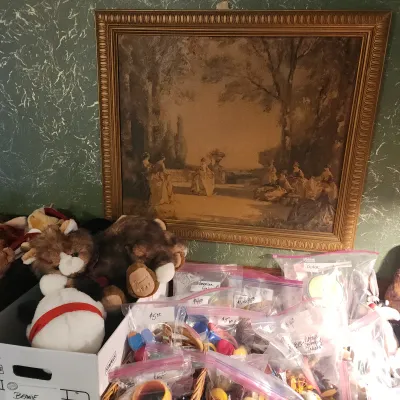 Sale Photo Thumbnail #104: Framed vintage sepia-toned classical landscape print hanging above a collection of plush stuffed animals and bagged small collectibles.
