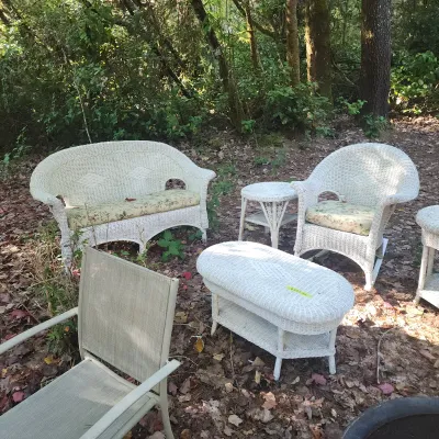 White wicker outdoor patio set including a sofa, armchair, side table, and oval coffee table with floral cushions, shown alongside a...
