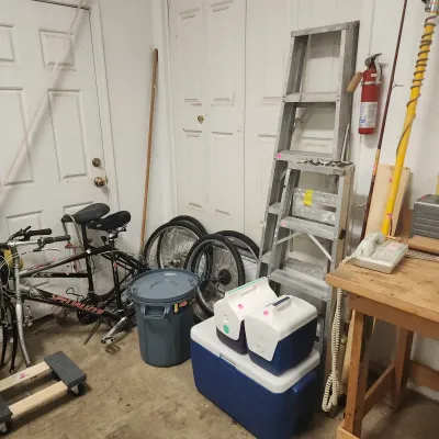 Collection of garage gear including a Specialized mountain bike, aluminum step ladders, various coolers, spare bicycle wheels, and a...