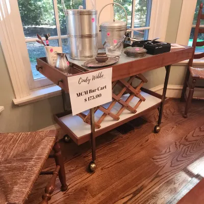 Sale Photo Thumbnail #113: Mid-century modern rolling wooden bar cart with brass legs, featuring an expandable wooden wine rack and various vintage barware accessories.