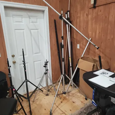 Assorted professional photography and lighting stands, including C-stands, boom arms, and lightweight aluminum tripod bases.