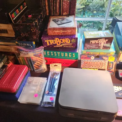 Collection of vintage board games, craft supplies, and stationery items, including TriBond, Guesstures, Scattergories, and MindTrap.