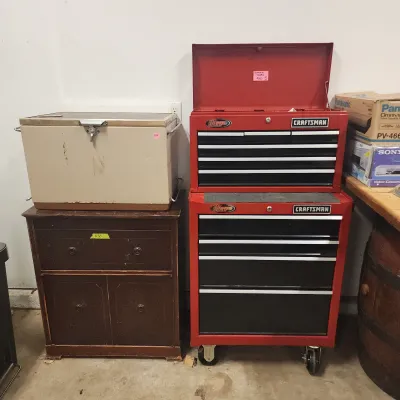 Sale Photo Thumbnail #120: Red Craftsman rolling tool chest combo with ball-bearing drawers alongside a vintage metal metal ice chest resting on a dark wood cabinet.