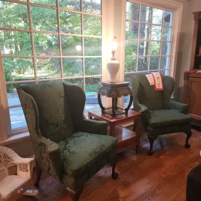 Sale Photo Thumbnail #108: Pair of Chippendale-style wingback armchairs upholstered in green damask fabric, featuring claw-and-ball feet, flanked by a wooden end table with a white ceramic lamp.