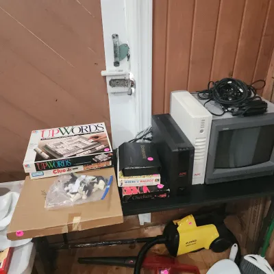 Sale Photo Thumbnail #122: Selection of vintage board games, electronics including an APC power unit and CRT monitor, alongside a yellow Eureka Mighty Mite vacuum.