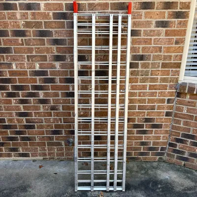 Sale Photo Thumbnail #77: Aluminum folding loading ramp with red protective end caps, leaning against a brick wall.