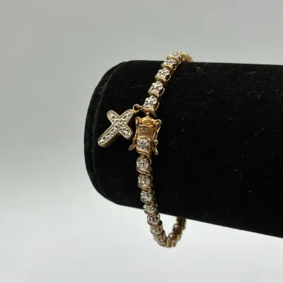Sale Photo Thumbnail #197: Gold-tone tennis bracelet featuring faux-diamond links and a small pave cross charm attachment.