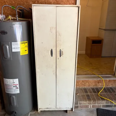 Sale Photo Thumbnail #75: Vintage white metal storage cabinet featuring two doors with black handles, showing surface wear and scuffs.