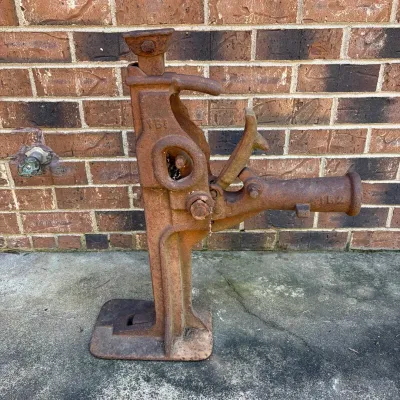 Sale Photo Thumbnail #67: Vintage heavy-duty cast iron mechanical jack with heavy surface rust and patina, posed outdoors against a brick wall.