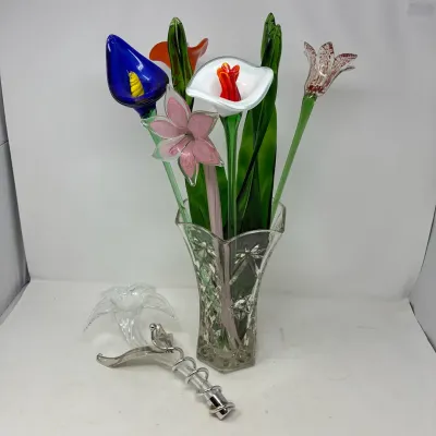 Sale Photo Thumbnail #178: Collection of colorful hand-blown art glass flowers arranged in a cut glass vase, accompanied by a clear glass flower and metal stand.