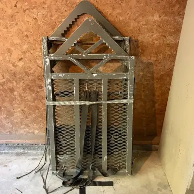 Sale Photo Thumbnail #42: Vintage olive green metal climbing tree stand with mesh platform and safety straps, showing scuffs and finish wear from use.
