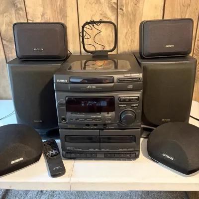 Sale Photo Thumbnail #131: Vintage Aiwa NSX-V21 shelf stereo system featuring a 3-disc CD changer, dual cassette deck, four surround sound speakers, loop antenna, and remote control.