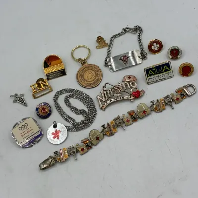 Sale Photo Thumbnail #194: Collection of nursing and medical-themed jewelry and pins, including an enameled charm bracelet, medical ID bracelet, caduceus pins, and various Arkansas medical organization lapel pins.