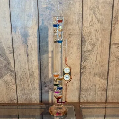 Sale Photo Thumbnail #51: Glass Galileo thermometer featuring multi-colored floating glass spheres, an attached liquid barometer tube, and inset analog clock and hygrometer dials.