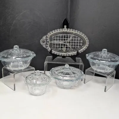 Sale Photo Thumbnail #127: Collection of clear pressed glass tableware featuring four covered bowls and a divided oval relish dish, displaying intricate beaded and faceted detailing.