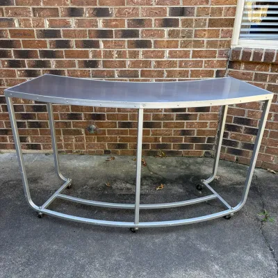 Sale Photo Thumbnail #79: Curved metal rolling bar or utility table featuring an aluminum frame and casters.