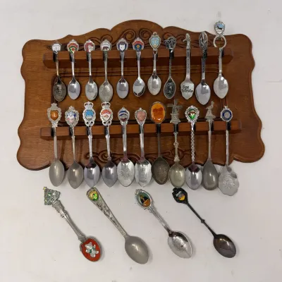Sale Photo Thumbnail #23: Vintage souvenir spoon collection, featuring state and travel-themed enamel and metal designs, displayed on a wooden rack.