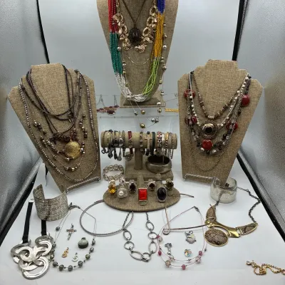Sale Photo Thumbnail #190: Collection of bohemian and statement fashion jewelry, including multi-strand beaded necklaces, silver-tone cuffs, textured rings, and various pendant necklaces displayed on burlap busts.