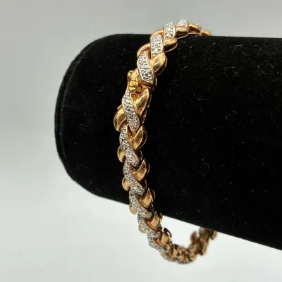 Sale Photo Thumbnail #196: Two-tone gold and diamond tennis bracelet featuring a braided, entwined link design displayed on a black velvet stand.