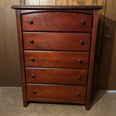 Sale Photo Thumbnail #3: Traditional cherry-stained five-drawer tall dresser with dark metal knobs and carved trim accents along the side posts.