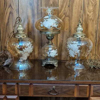 Sale Photo Thumbnail #5: Trio of vintage amber glass light fixtures, including a Gone with the Wind-style table lamp and a matching pair of hanging swag lamps, all featuring white floral etched details and brass hardware.