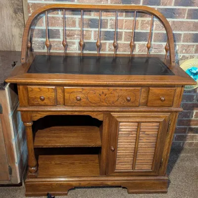 Sale Photo Thumbnail #49: Traditional solid oak dry bar cabinet featuring a black inset tile top, spindle gallery back, carved center drawer, and lower louvered door storage.